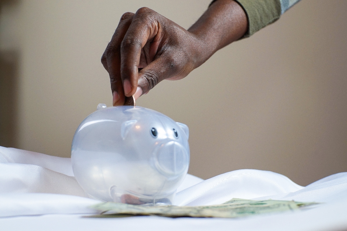 Image of a hand putting money into a clear piggy bank.