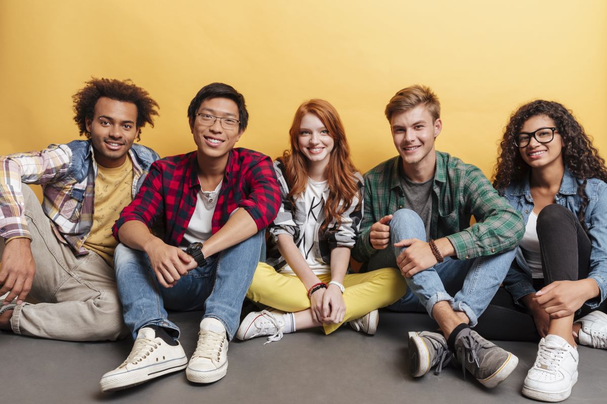 Group of five teens - two young women and three young men - facing the camera and smiling.