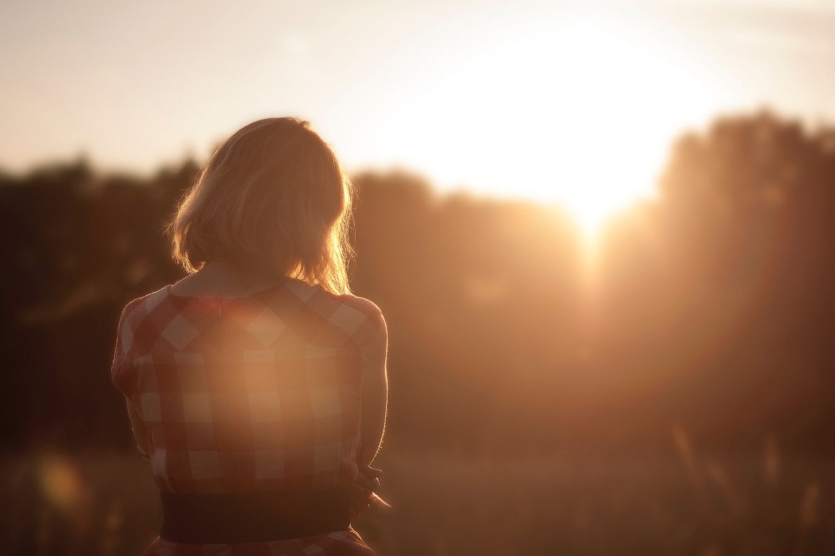 A young person sits on a wall at sunset.