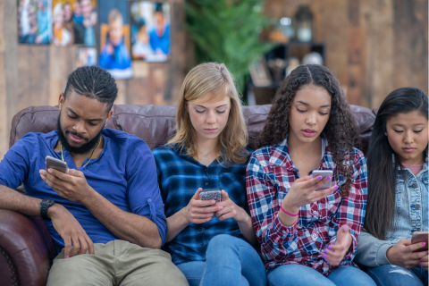 Diverse teens on their phones sitting next to one another. 