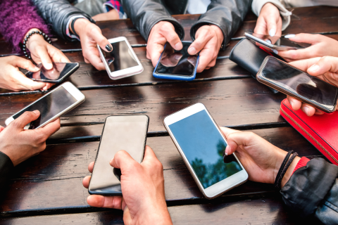 A group of people in a circle are holding their phones towards the center of the group.
