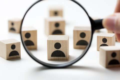 Magnifying glass over a group of toy blocks printed with icons of people.