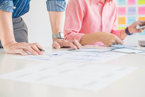 Two people working with papers laid out on a table and colorful sticky notes in the background