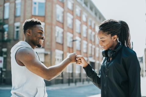 African American young man and young woman outside giving each other a fist-bump as they meet.