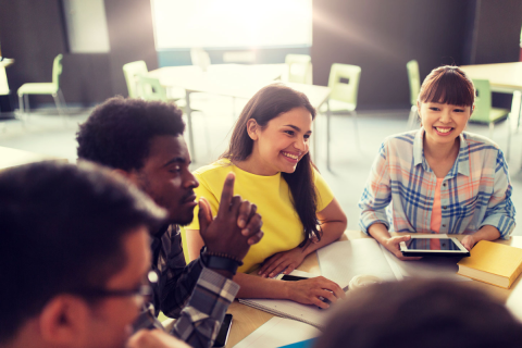 Five diverse teens sitting at a table in a classroom setting.