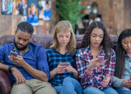 Diverse teens on their phones sitting next to one another. 