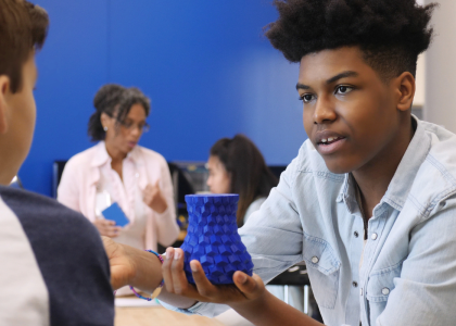 Teen holding up a piece of art to another youth.