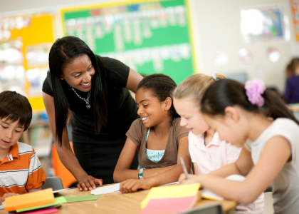 A teacher is standing over four youth working at a shared desk