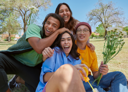 Four smiling youth sitting on grass.