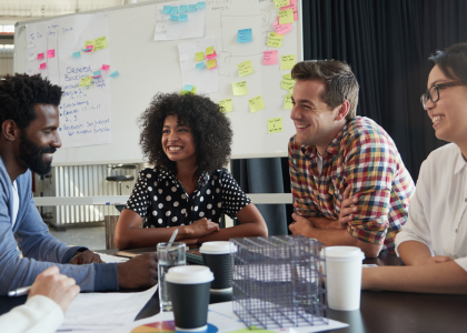 Four people having a meeting around a conference table in front of a white board. 