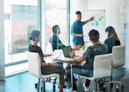 4 people sitting at a desk looking at someone giving a presentation