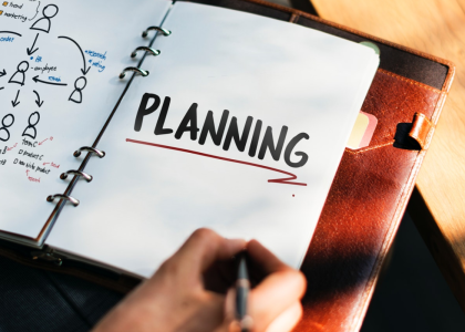 Picture of a hand writing in a spiral notebook with a flowchart on the left page and planning written on the right page.