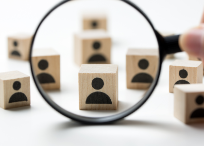 Magnifying glass over a group of toy blocks printed with icons of people.