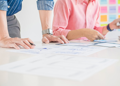 Two people working with papers laid out on a table and colorful sticky notes in the background