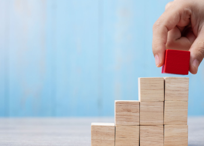 Photo of 8 wooden blocks stacked in an unfinished triangle. A hand is placing another block, painted red, on the top to finish the triangle.