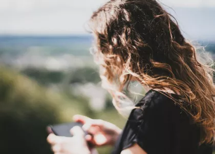 Teenage girl standing alone outside looking at her phone.