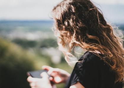 Teenage girl standing alone outside looking at her phone.