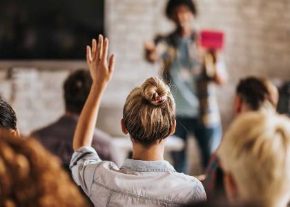 Image of young female raising hand in a group setting.