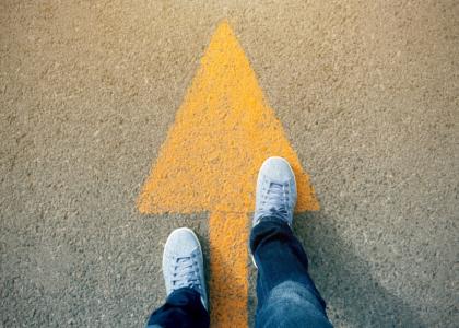 Person standing on yellow arrow on the ground. The arrow points forward.