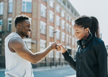 African American young man and young woman outside giving each other a fist-bump as they meet.