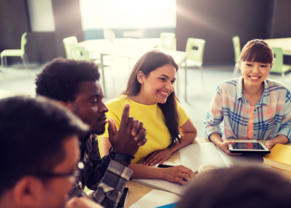 Five diverse teens sitting at a table in a classroom setting.