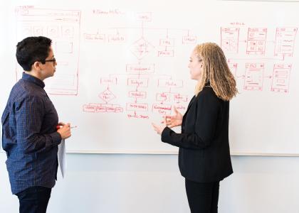 Two professionals, one man and one woman, standing in front of a whiteboard.
