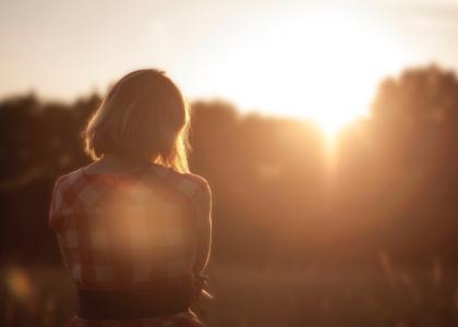 A young person sits on a wall at sunset.