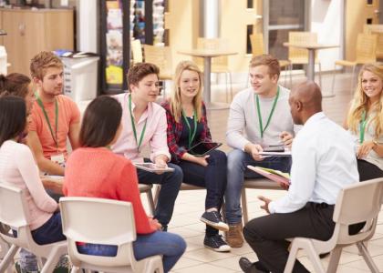 Group of young men and women sitting in chairs in a circle engaging in conversation with an instructor.