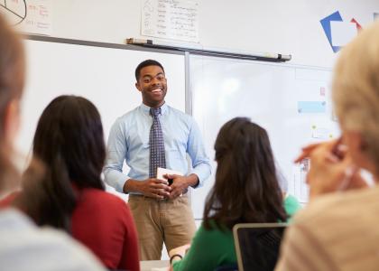 A man is standing at the front of a classroom coaching a group of adults.