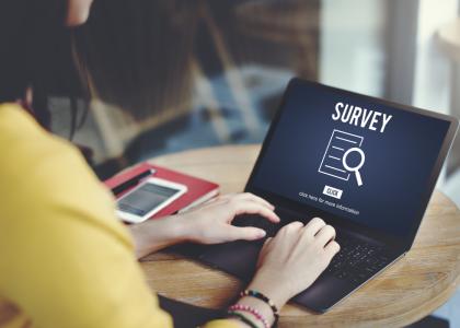 A young woman sits at a laptop with a Survey displayed on the screen.