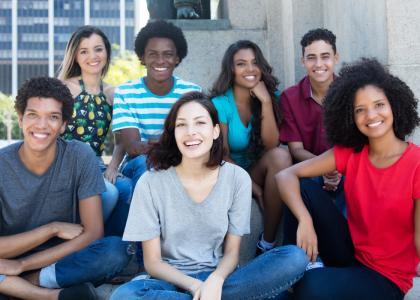 Diverse group of seven teens, three young men and four young women. They face the camera and are smiling.
