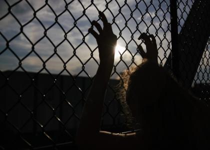 Young woman holding on to a chain link fence.